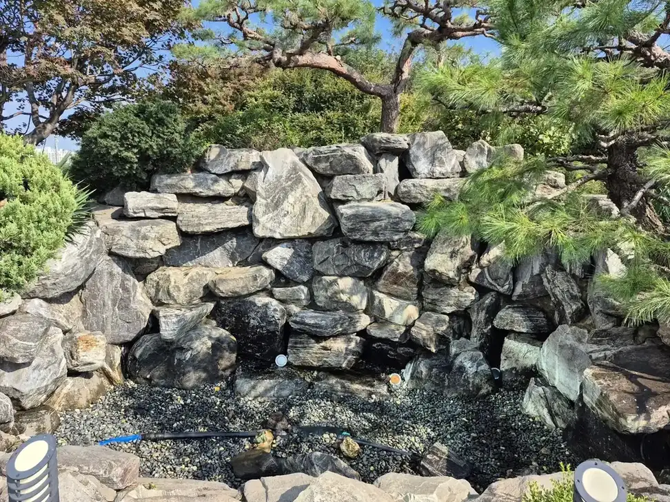 암석 벽 앞 자갈이 깔린 건조한 연못 바닥 시공 전